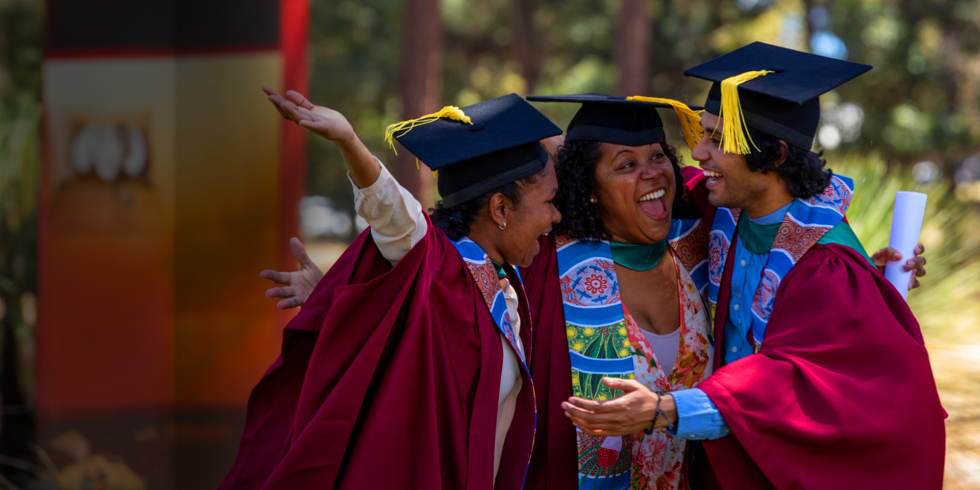 Three graduating indigenous Australians celebrating in academic regalia clothing